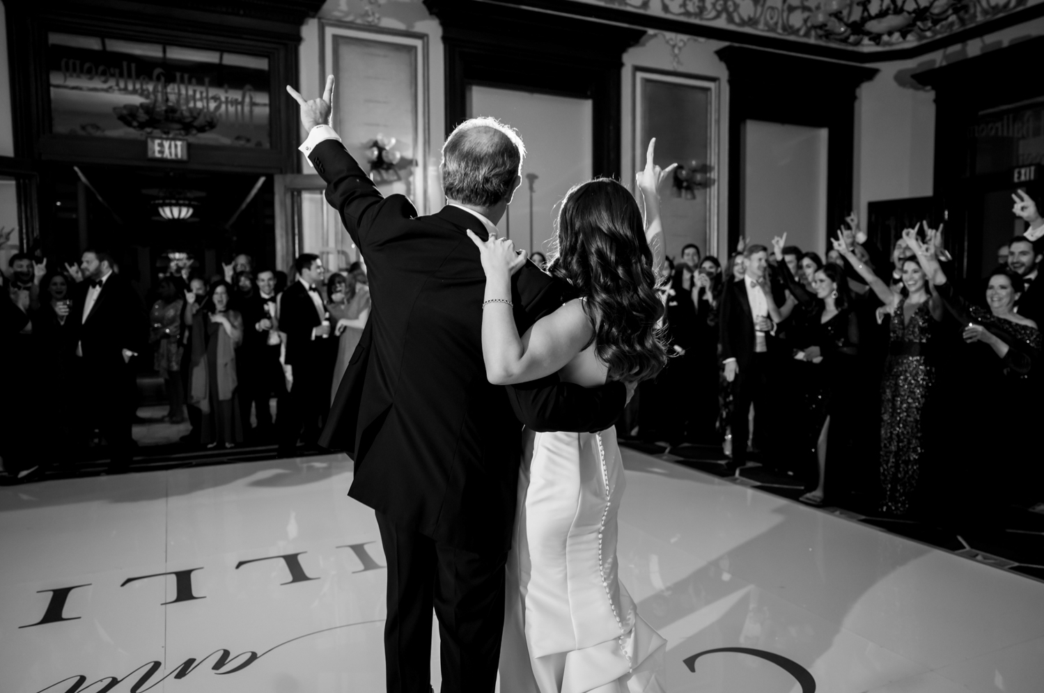 The bride and her dad face the crowd during their first dance and hold up the "hook-em" hand sign from The University of Texas at Austin.