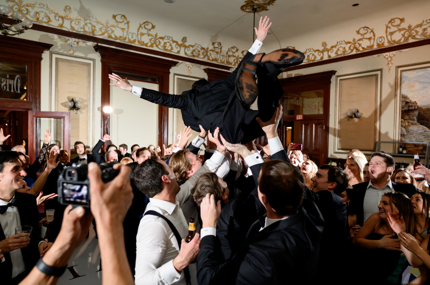 The groom being lifted by the crowd, holding his hands in the air.