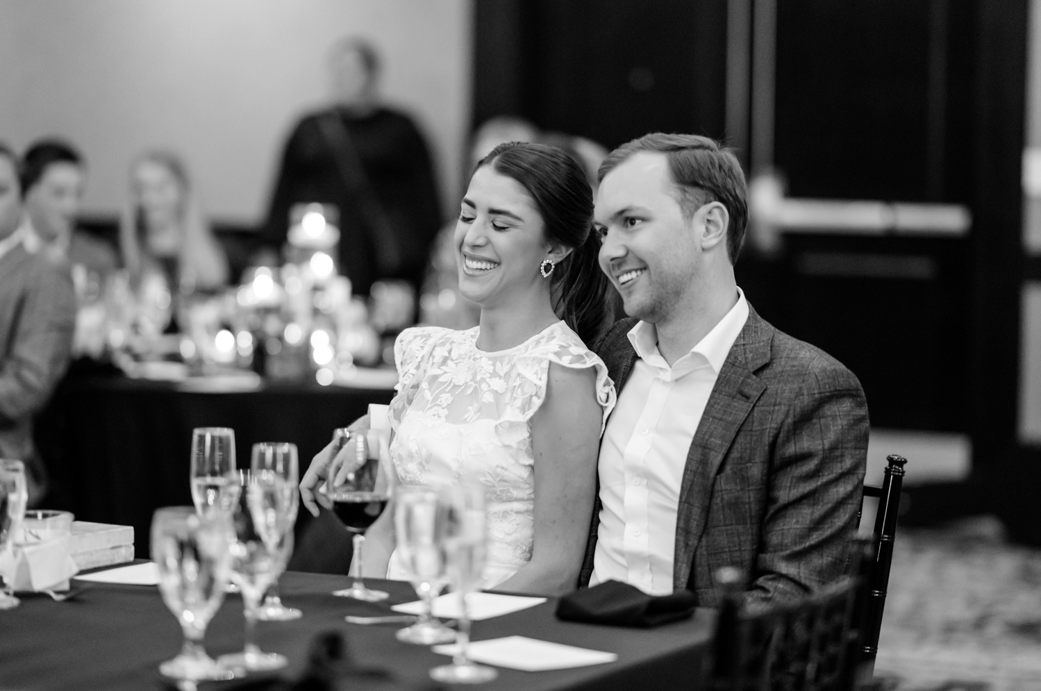 The bride and groom smile as they listen to toasts at their rehearsal dinner