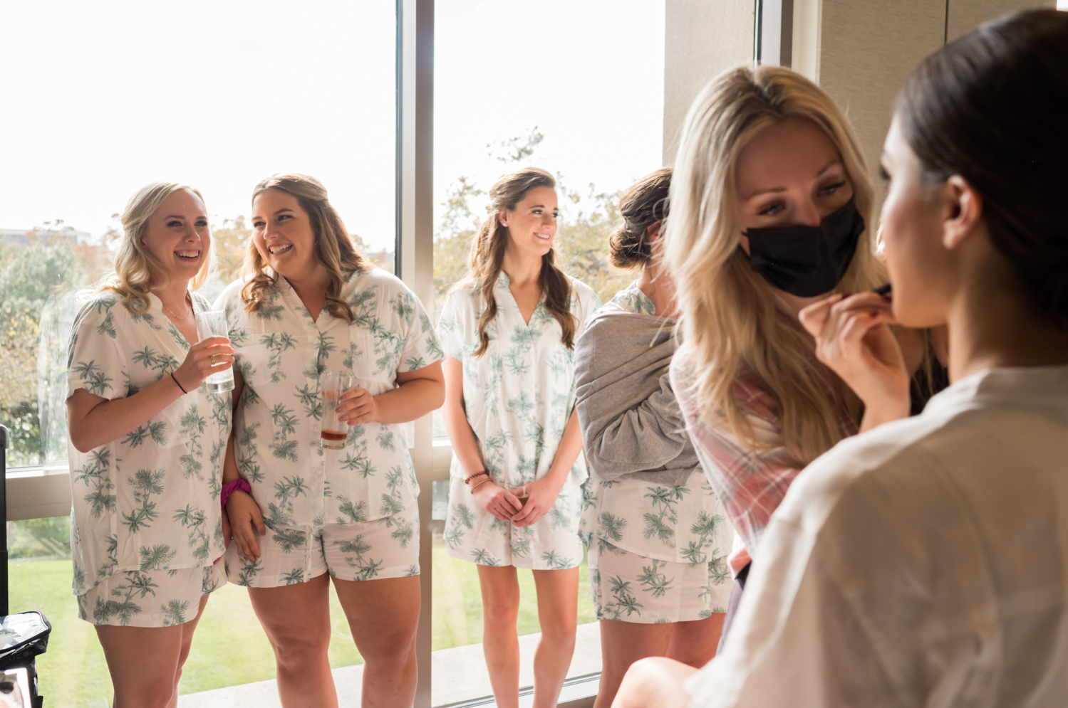 The bridesmaids smile as they watch the bride get her makeup done on the big day