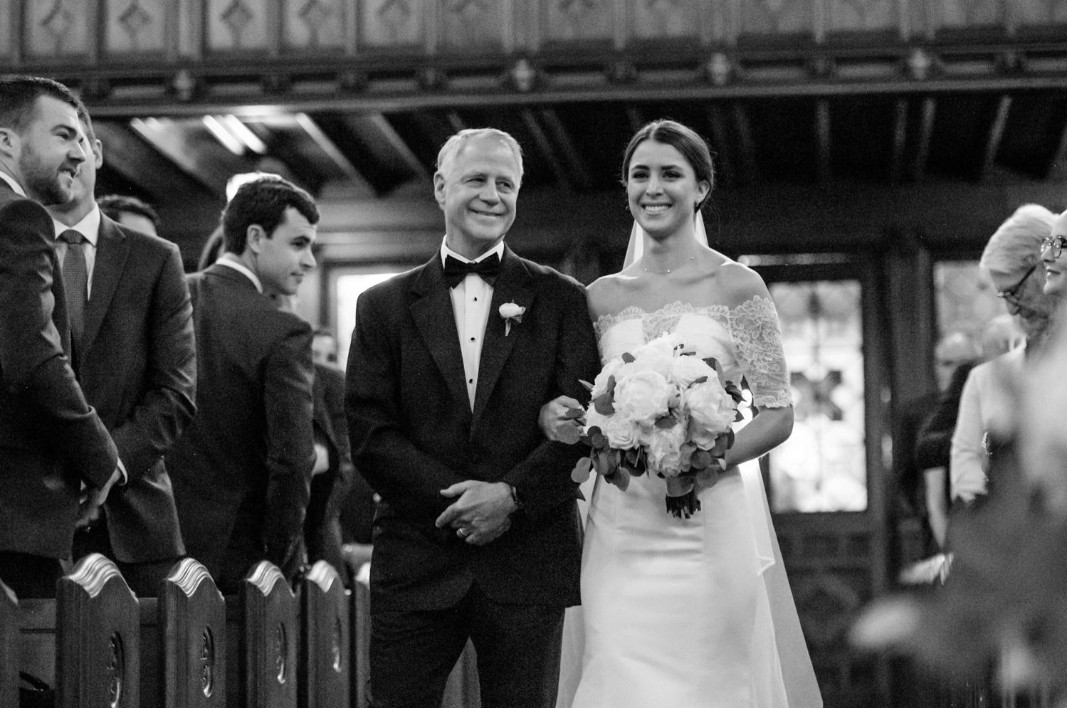 The bride and her father smile as they walk down the aisle together