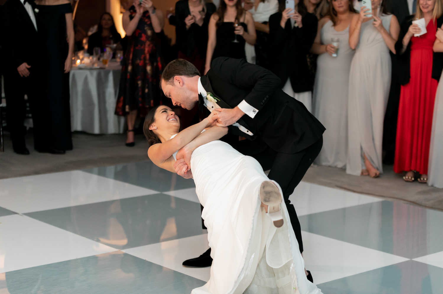 The groom dips the bride during their first dance and they smile at each other.