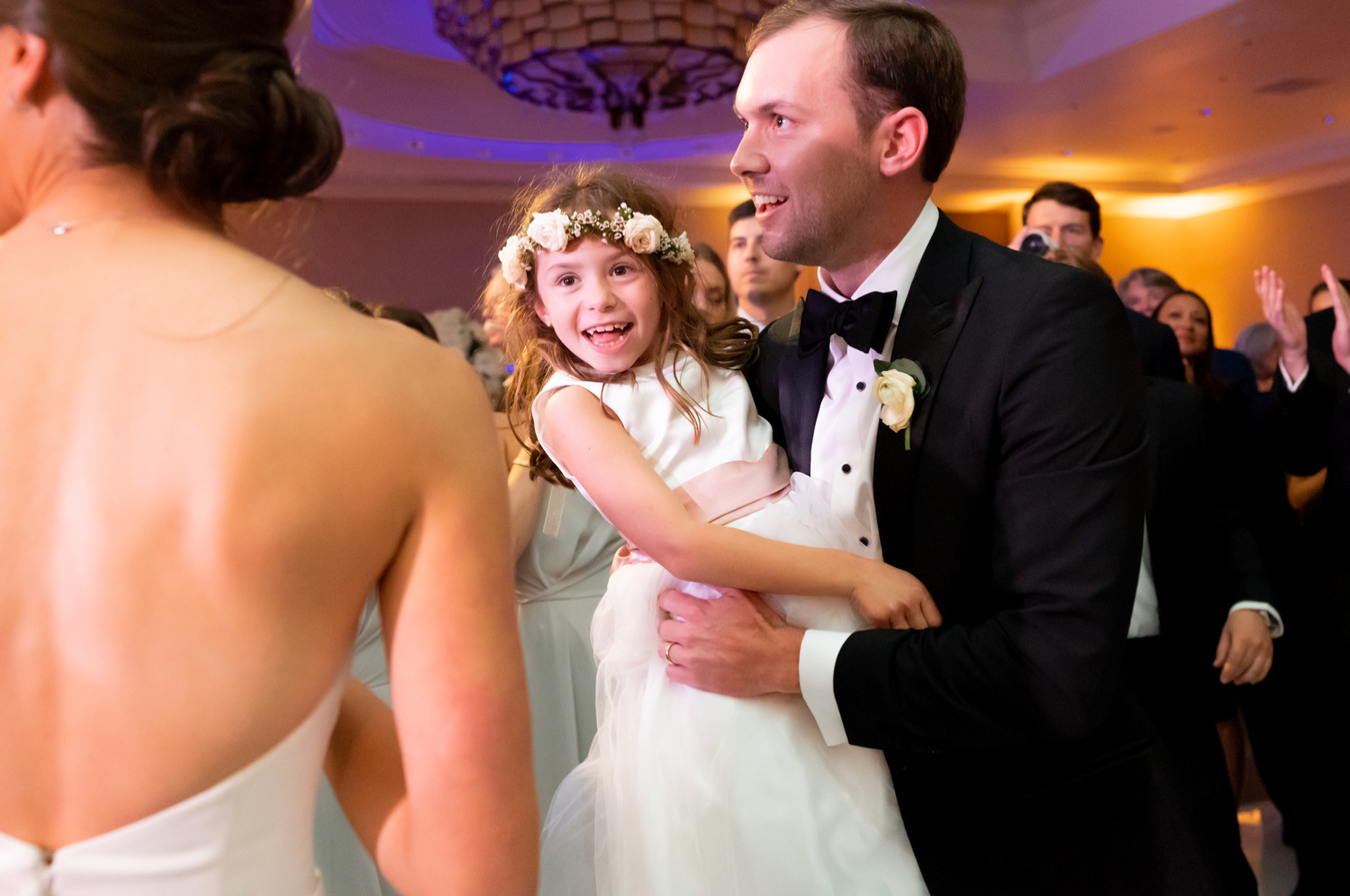 The groom holds the flower girl and they dance to the music.
