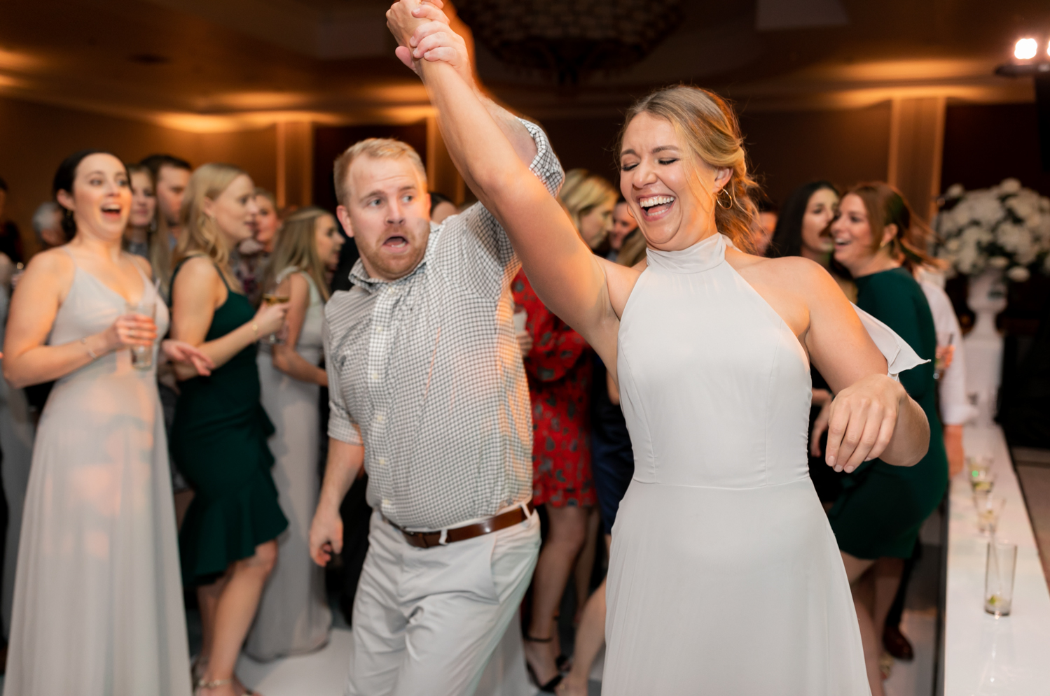 A guest spins one of the bridesmaids on the dance floor and they both laugh.