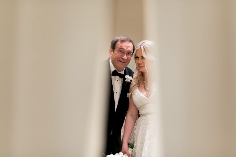 bride and her father peeking through the curtains