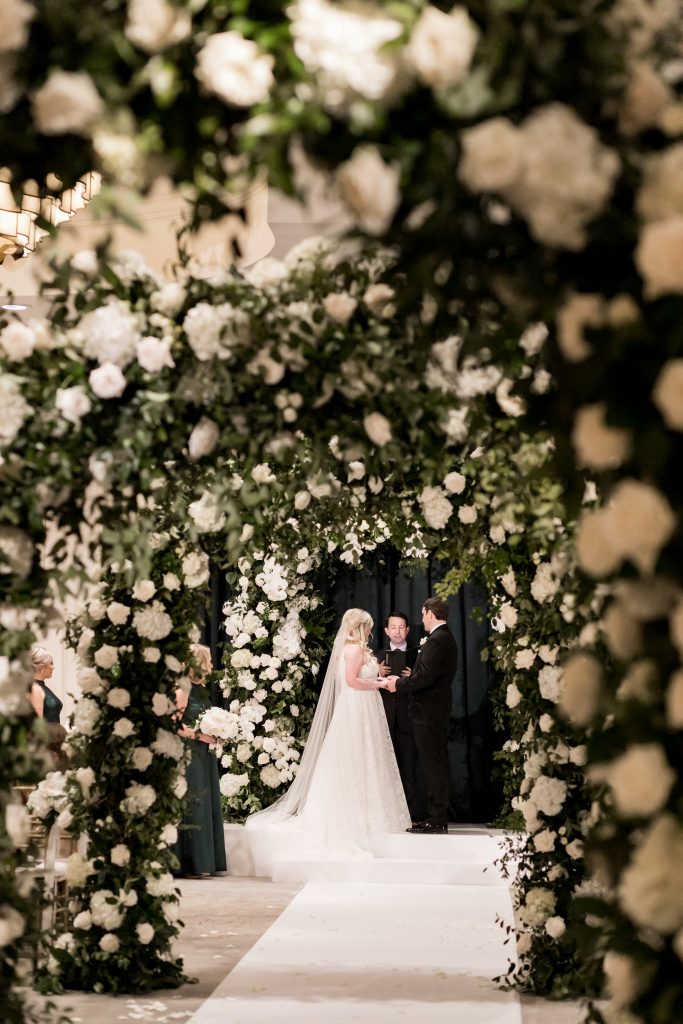bride and groom at the altar with floral archways lining the aisle
