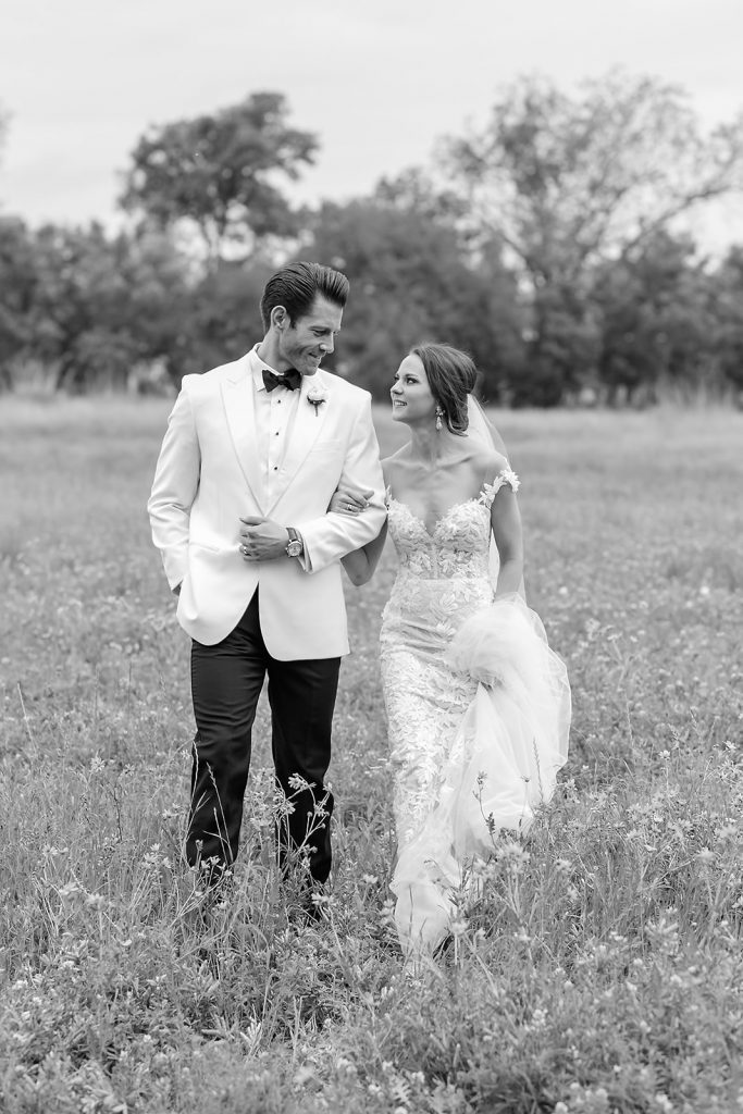 bride and groom looking at each other as they walk through a field of wildflowers