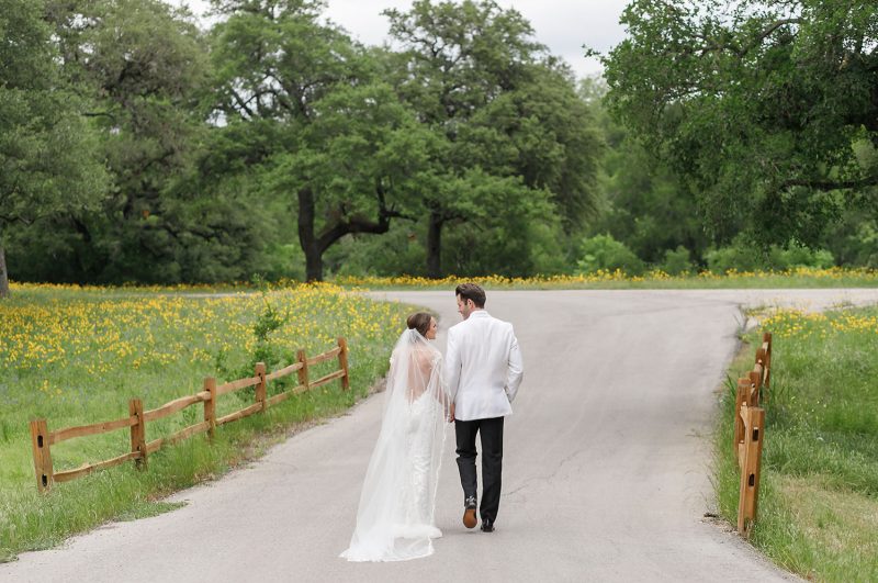 bride and groom walking away toward a field of yellow wildflowers