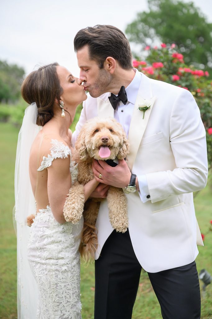 bride and groom kissing as they hold their puppy