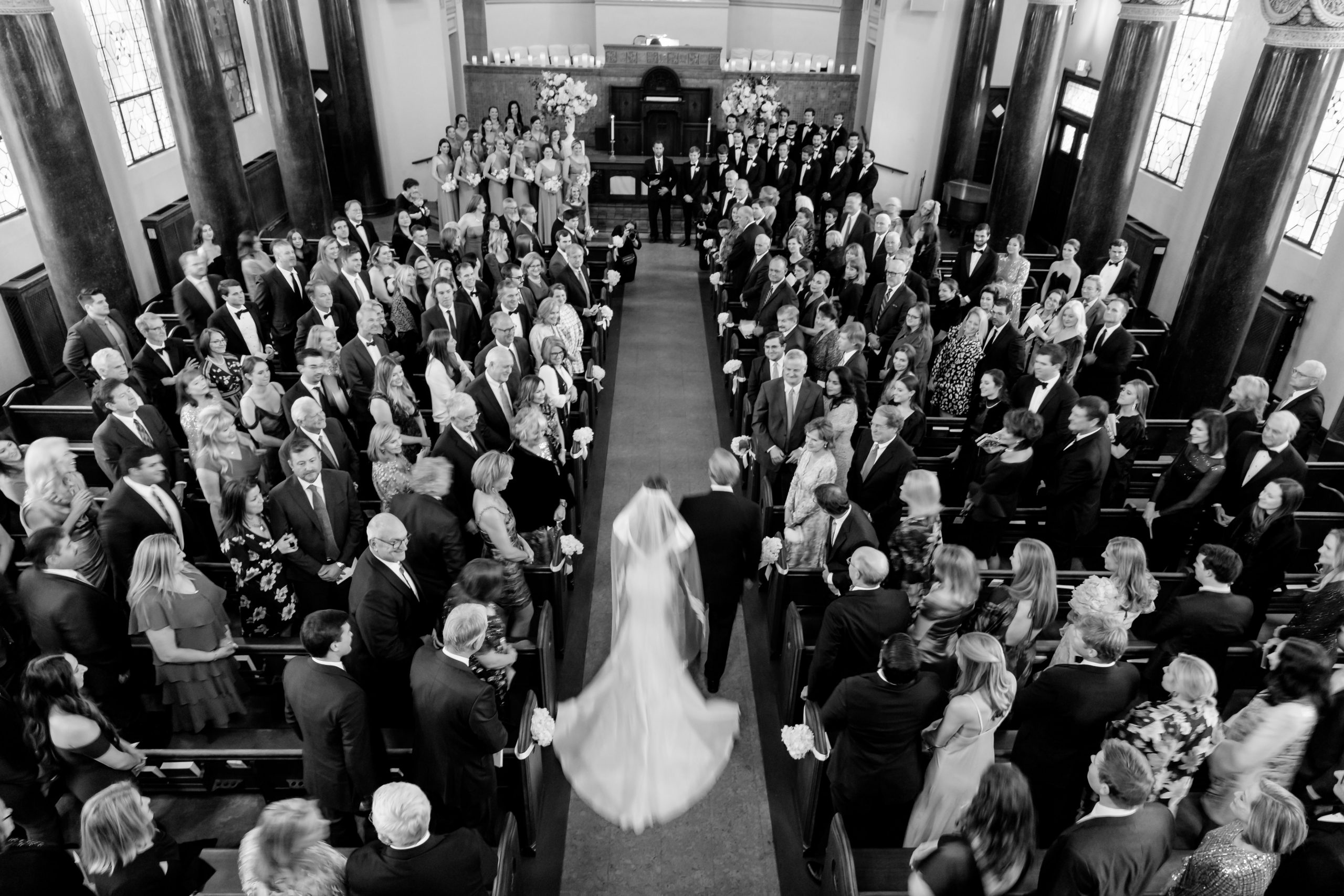 Black and white overhead image of a bride walking through guests during the ceremony