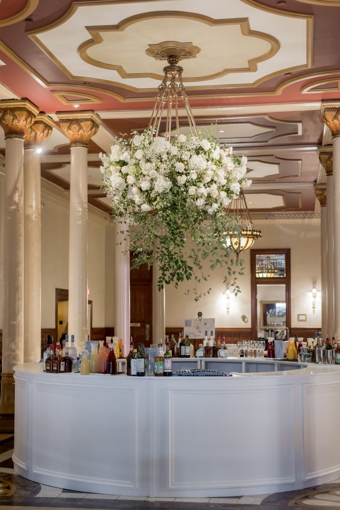 Wedding bar setup on The Driskill mezzanine beneath floral arrangements and chandeliers