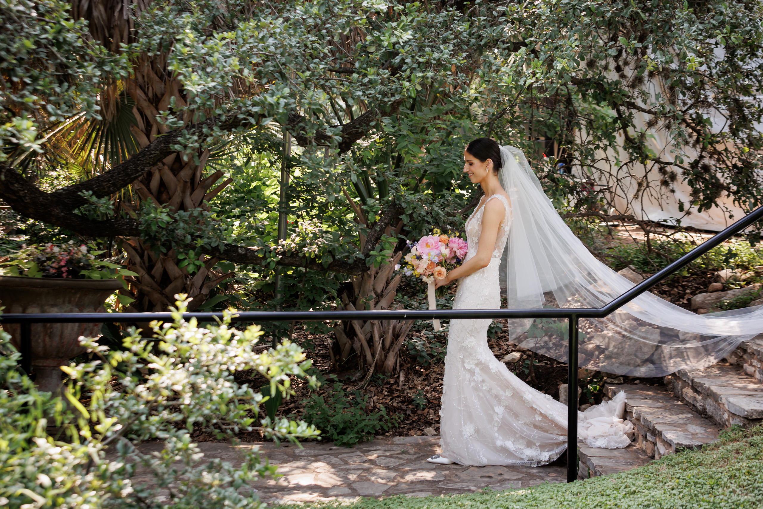 Bride walking through the wooded gardens at Laguna Gloria with a colorful spring bouquet