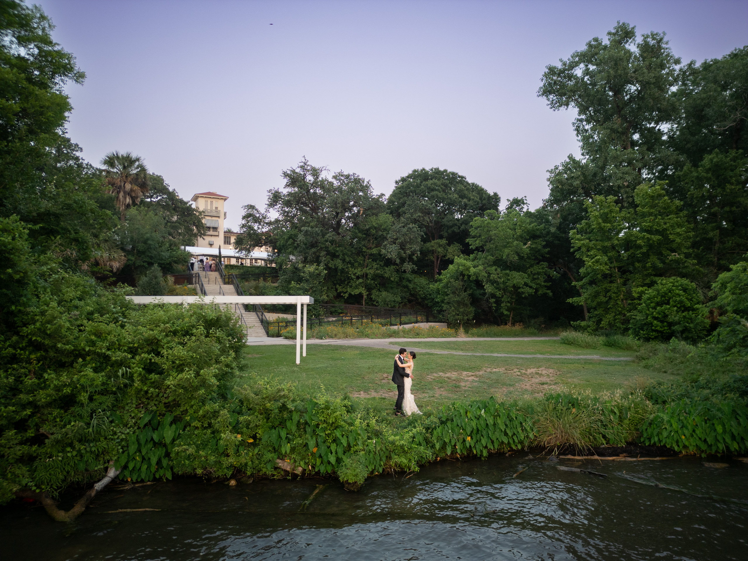 Bride and groom photographed across the water on the lakeside grounds at Laguna Gloria