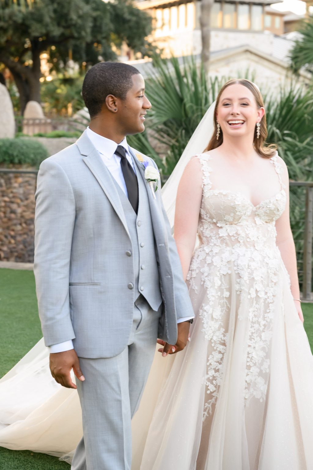 Kelli and Reggie sharing a joyful moment outdoors, with the bride in a stunning Galia Lahav gown and the groom in a tailored gray tuxedo, exuding effortless elegance.