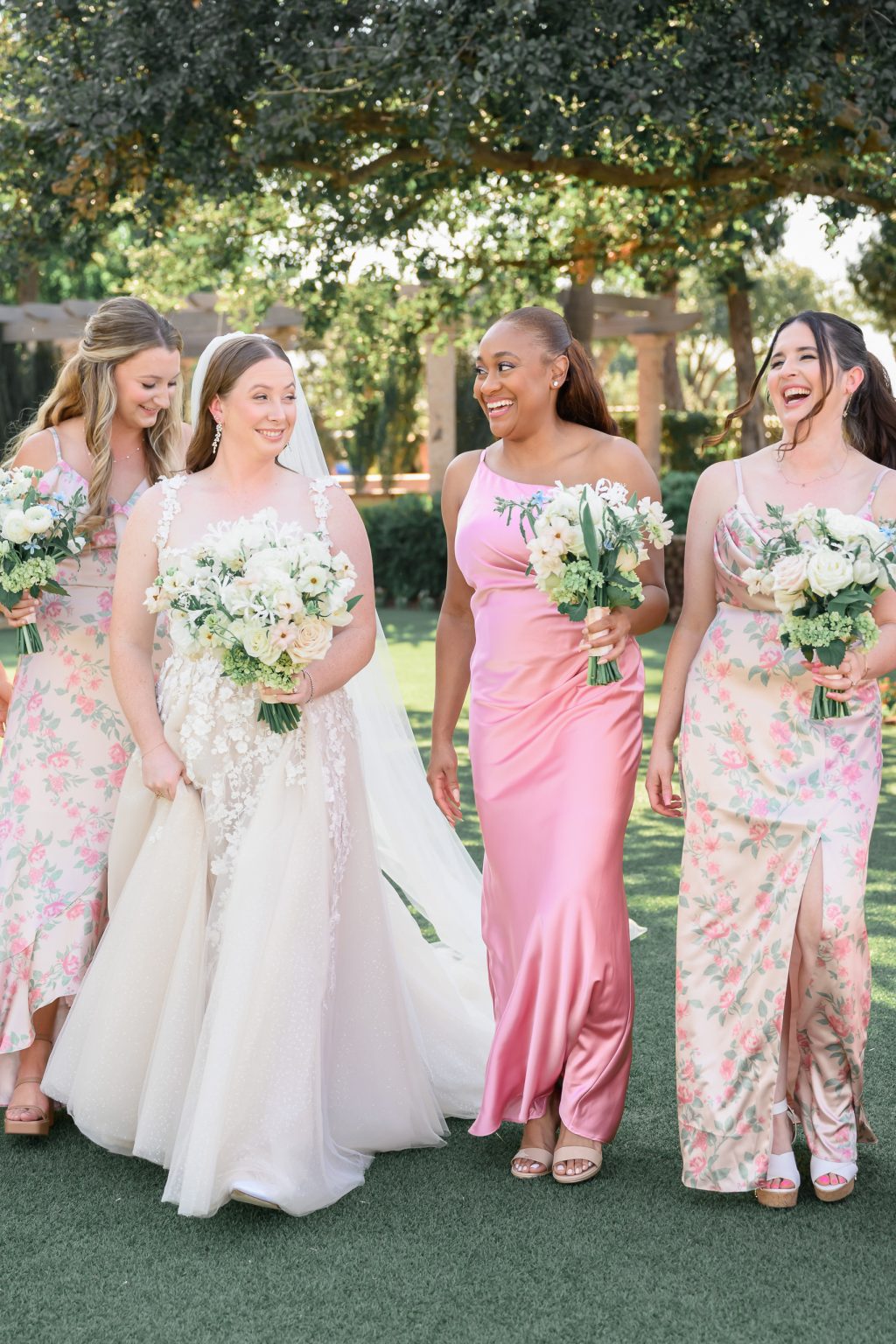 Kelli’s bridesmaids standing together in a mix of blush pink and floral-patterned gowns, radiating joy and elegance