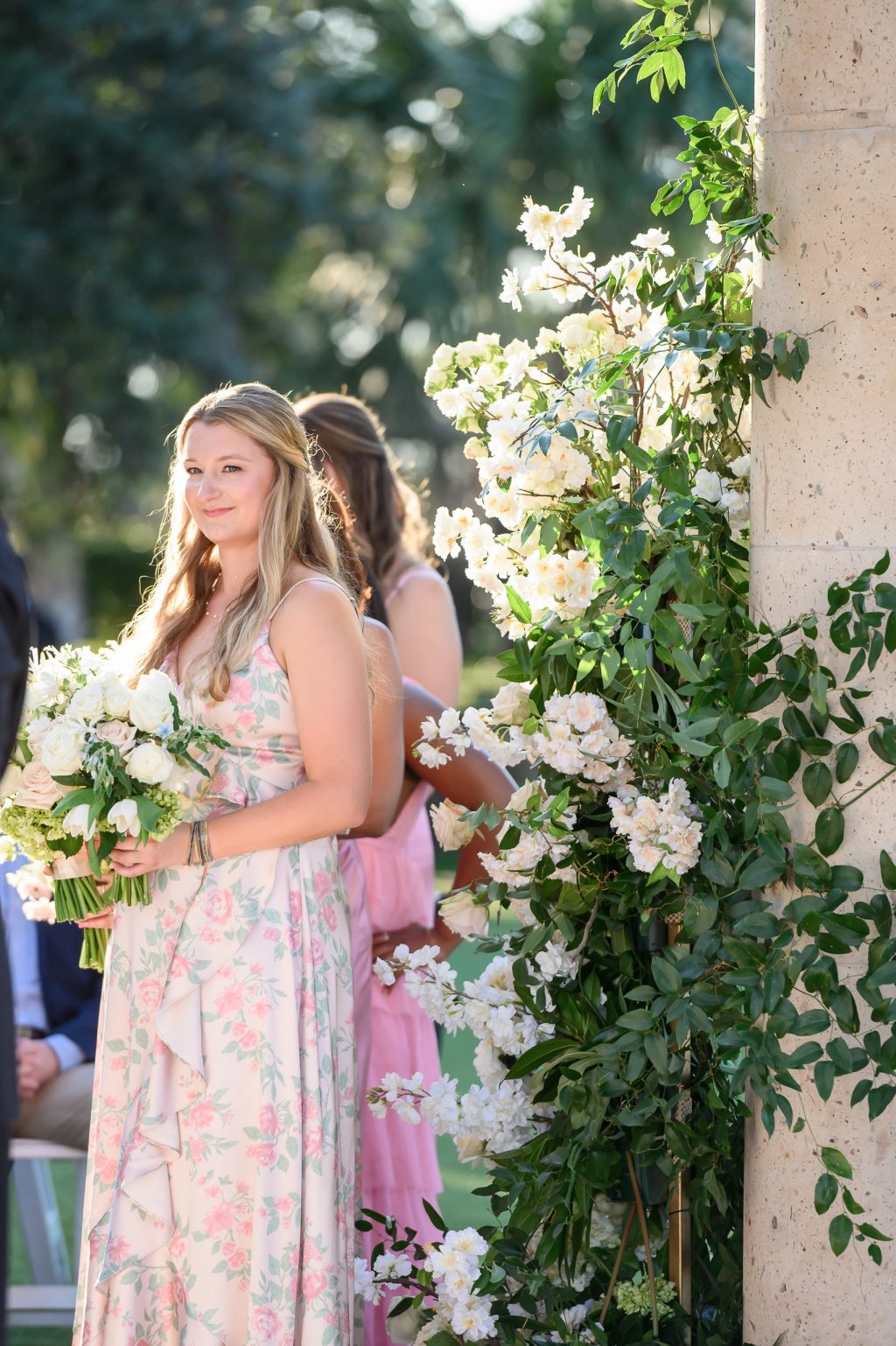 A bridesmaid delivering a heartfelt toast, standing against a backdrop of lush greenery and floral arrangements.