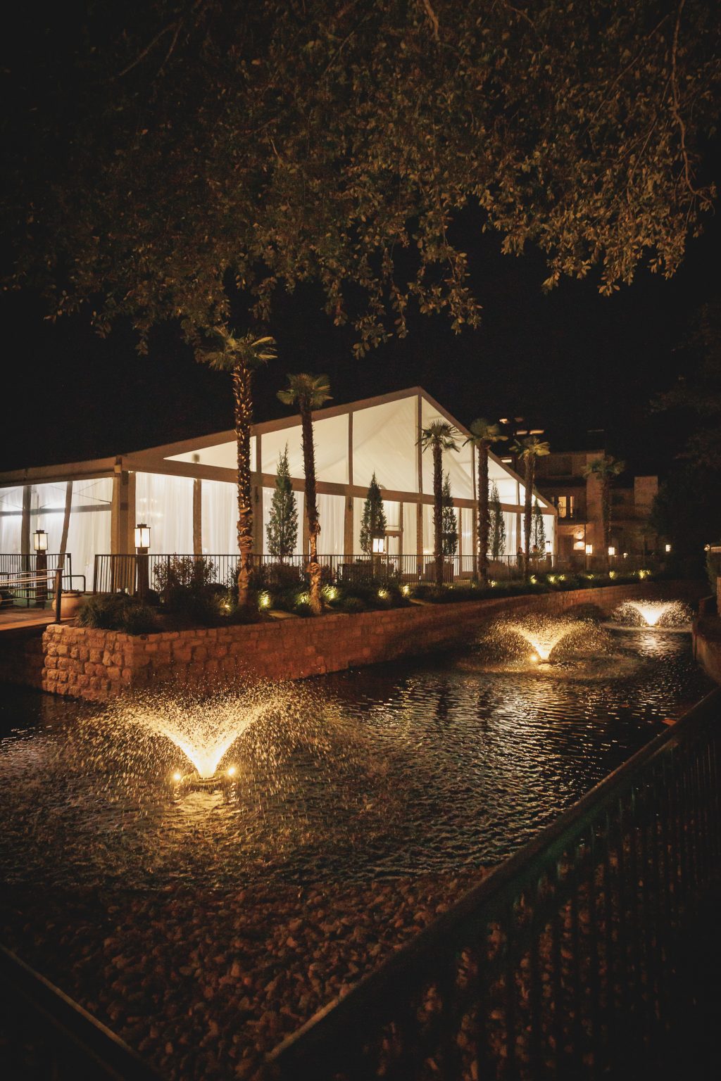 A breathtaking aerial view of a lakeside wedding reception at Horseshoe Bay Resort, showcasing an elegant white tent glowing under the Texas night sky. Nestled along the waterfront, the reception space blends luxury wedding ambiance with the natural beauty of the Hill Country. Inside, warm candlelight and sophisticated decor create a refined yet inviting atmosphere, perfect for couples seeking a high-end destination wedding in Texas.