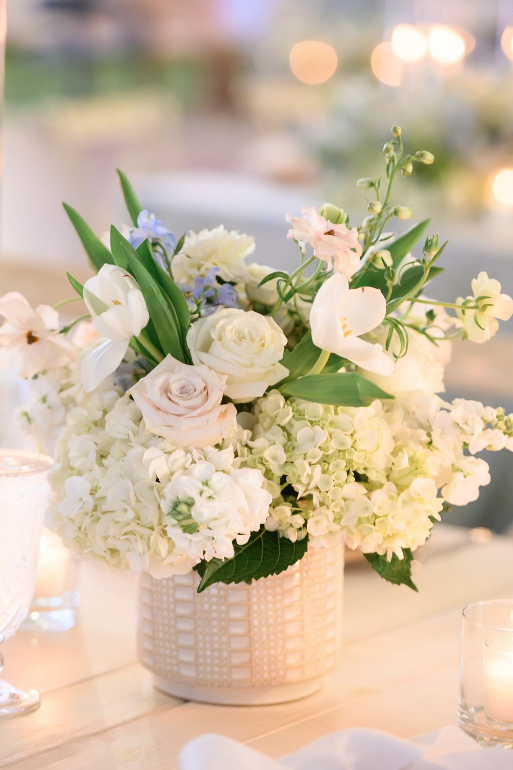 A lush wedding centerpiece featuring blush roses, white hydrangeas, and floating candles, creating a romantic and timeless reception aesthetic.