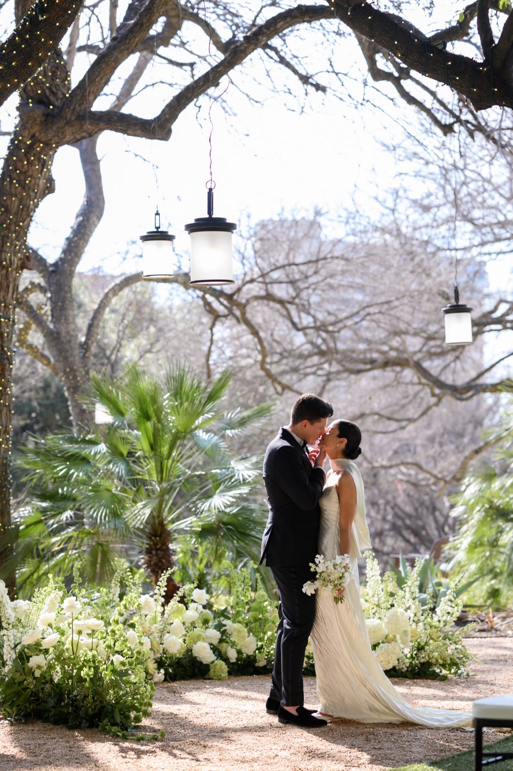 Bride and groom kissing beneath the trees during spring wedding portraits at Four Seasons Austin