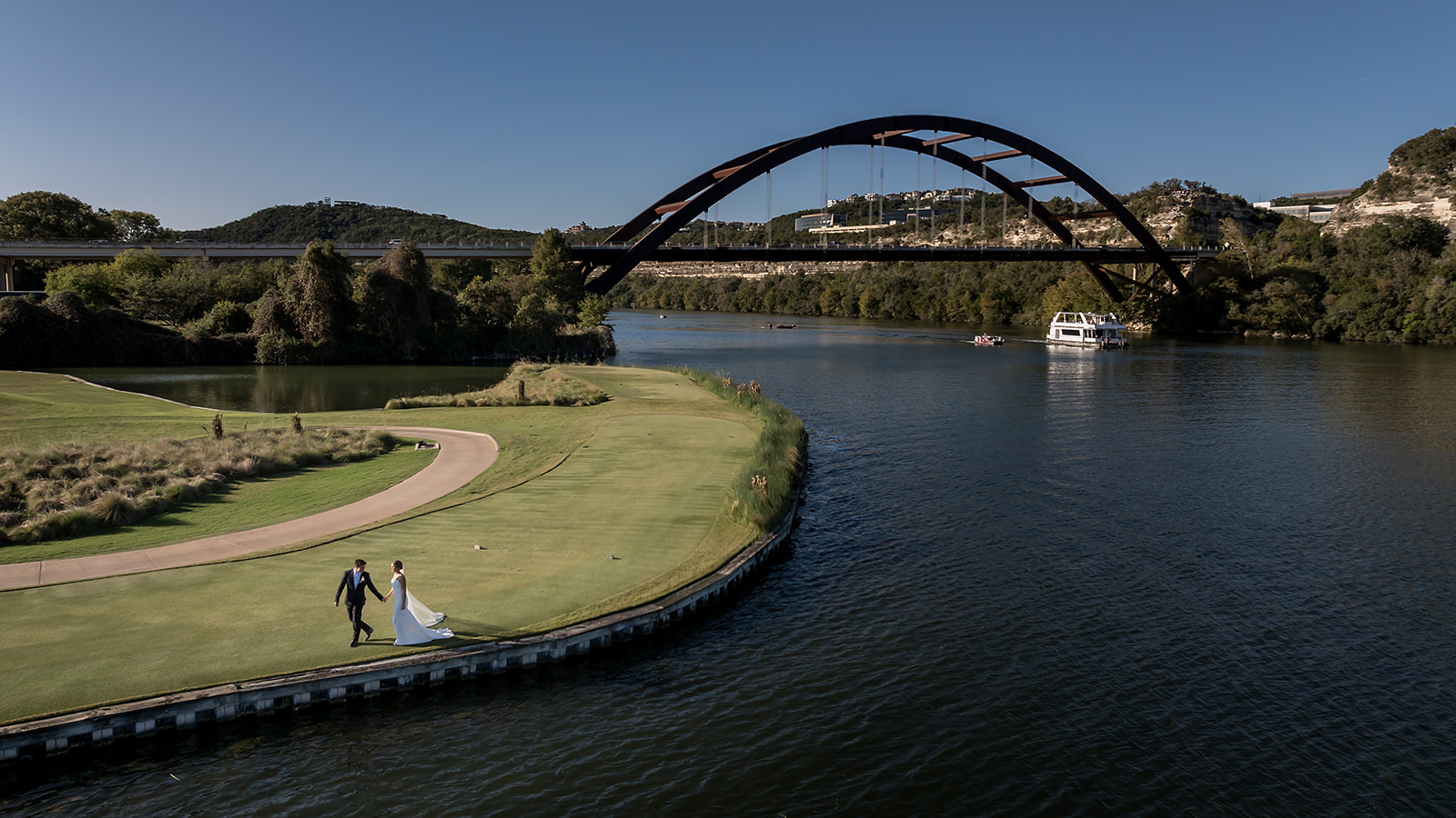 Bride and groom walking hand in hand on the golf course at Austin Country Club, with the Pennybacker Bridge and Lake Austin in the background