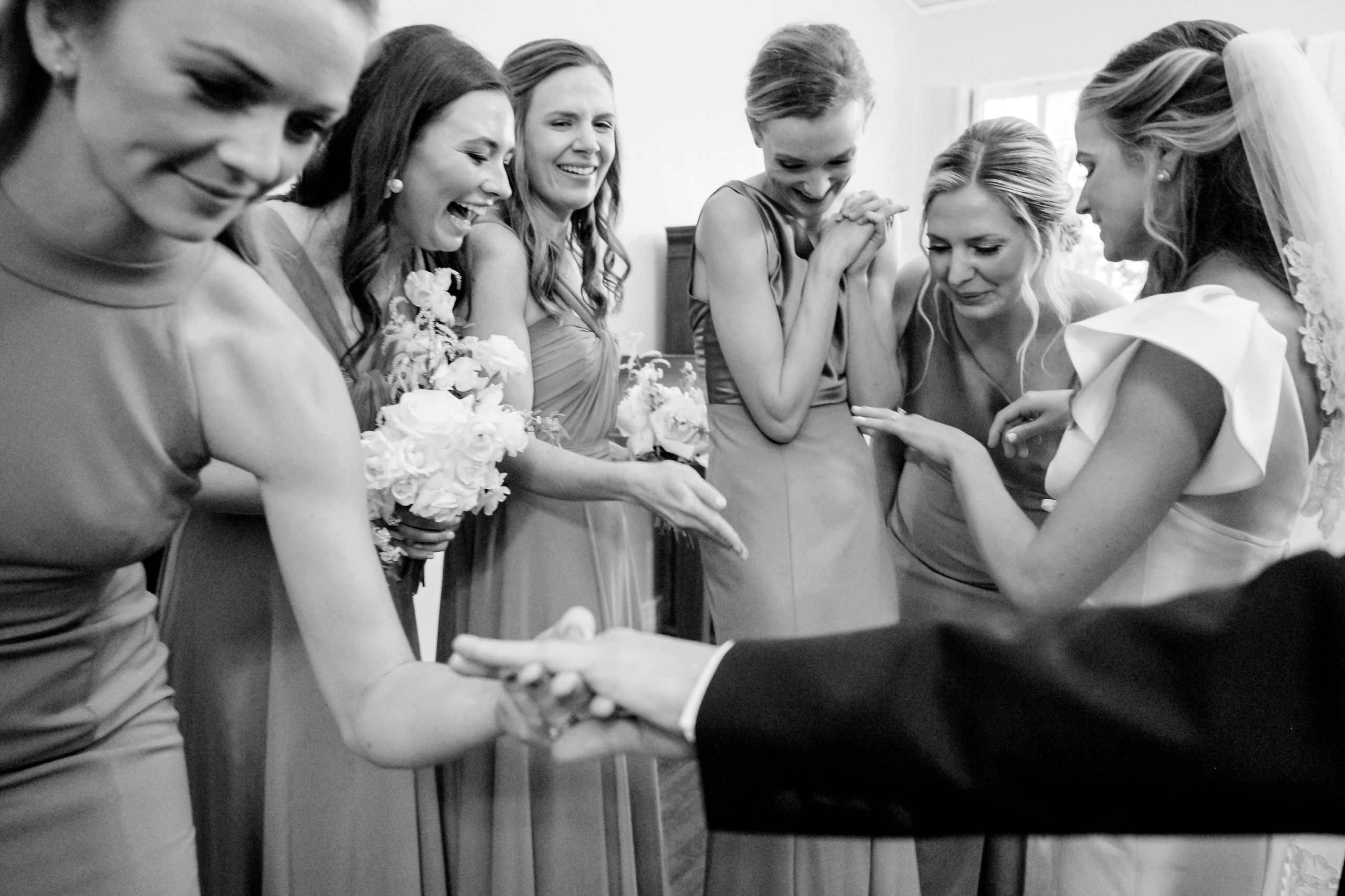 Black and white candid photo of a bride laughing with bridesmaids and family