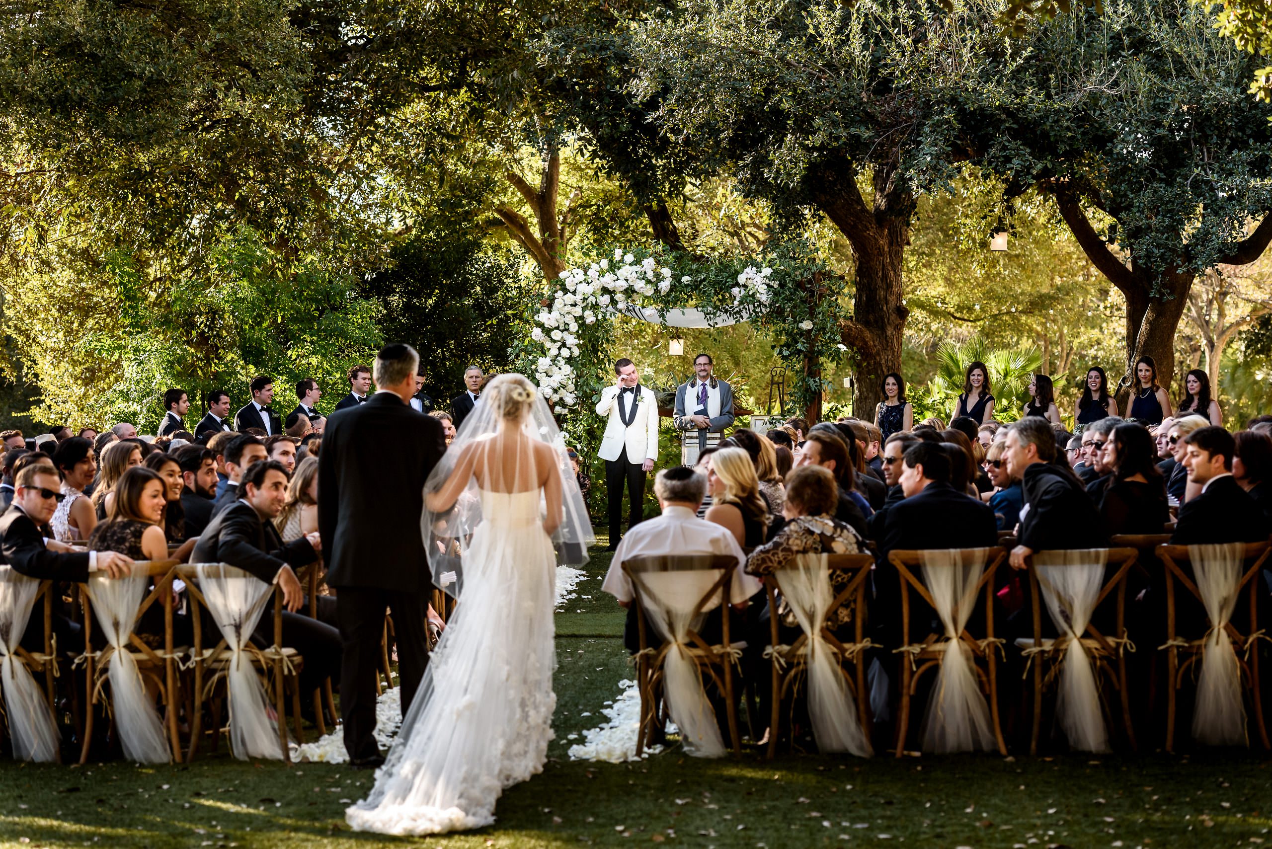 Outdoor wedding ceremony beneath large oak trees with the bride and groom at the altar