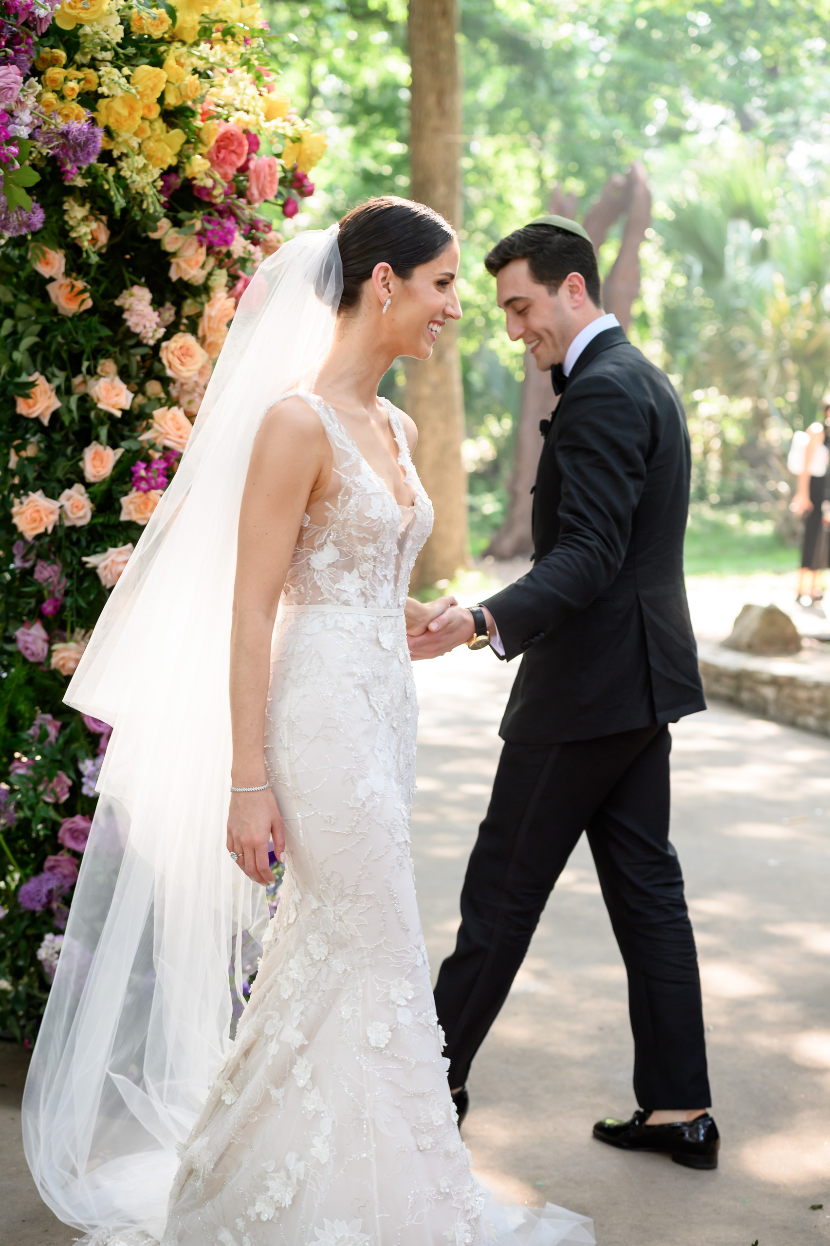 Bride and groom sharing a candid moment beside colorful wedding flowers during an outdoor ceremony