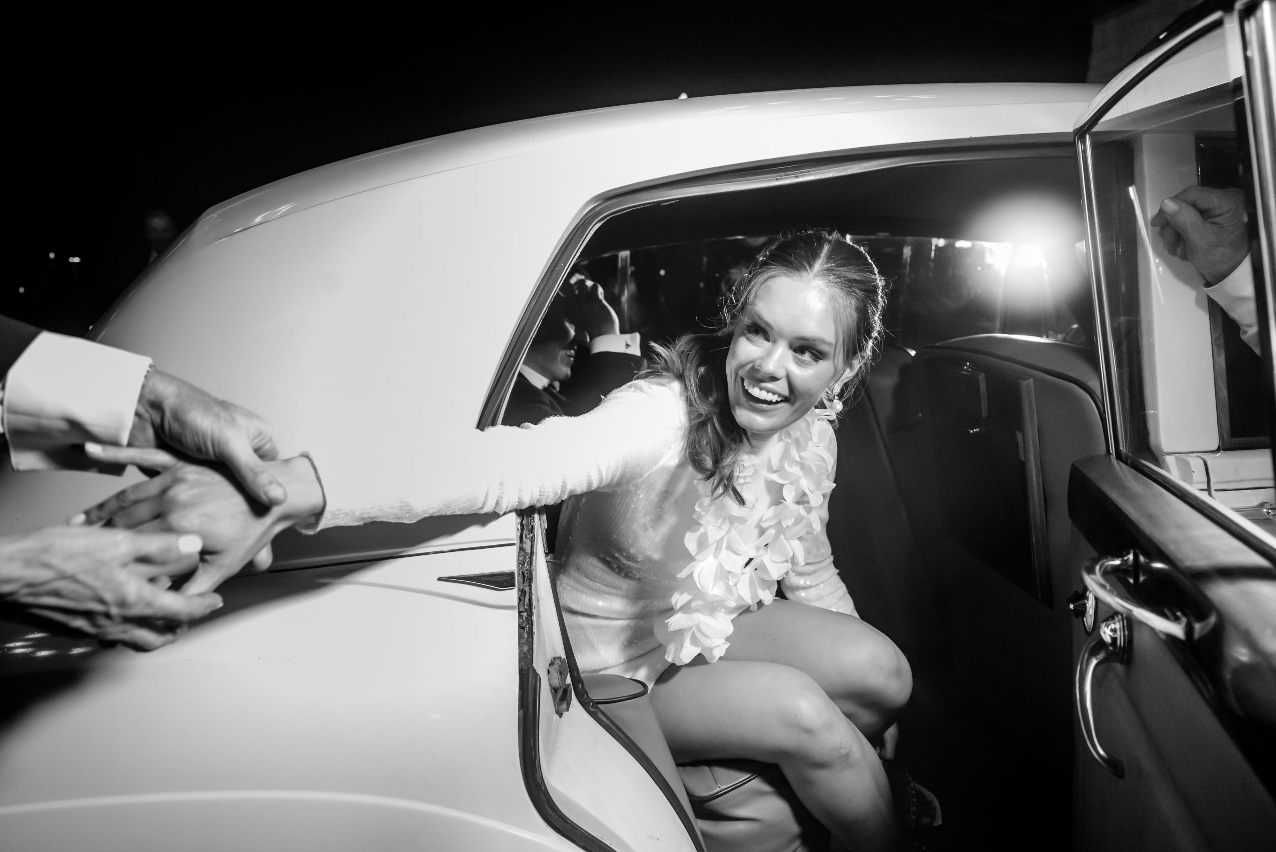 Black and white candid image of a bride smiling from inside a classic getaway car