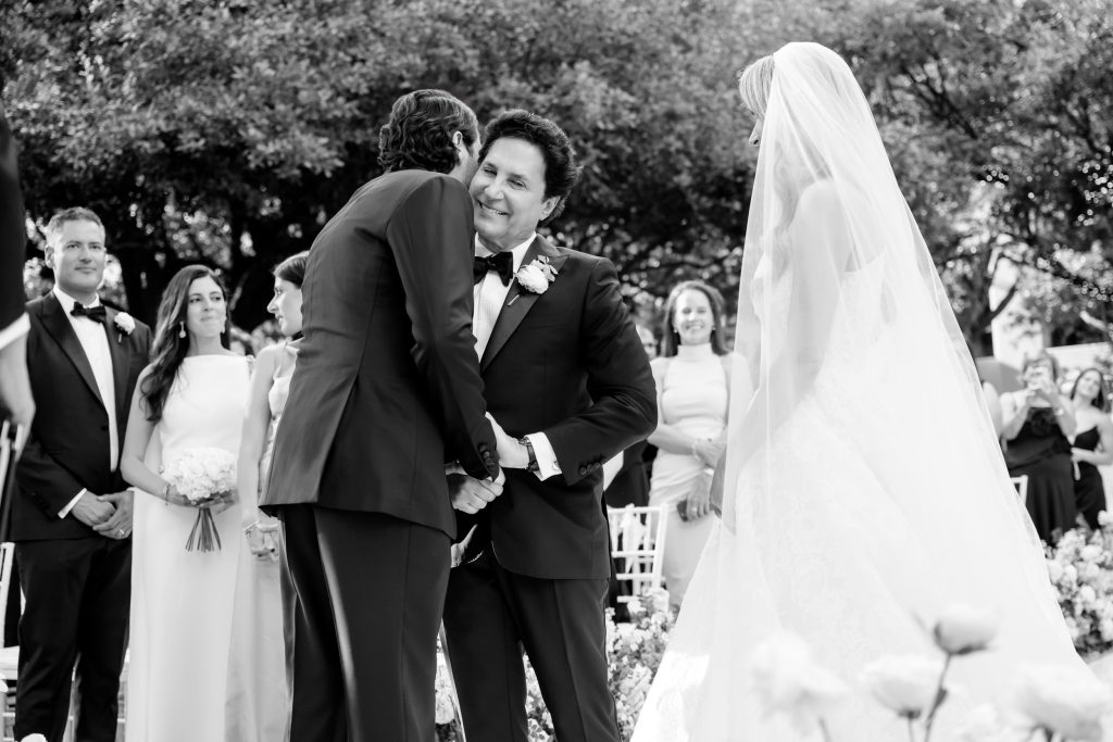 Black and white candid moment of the father of the bride greeting the groom during an outdoor Four Seasons Austin wedding ceremony