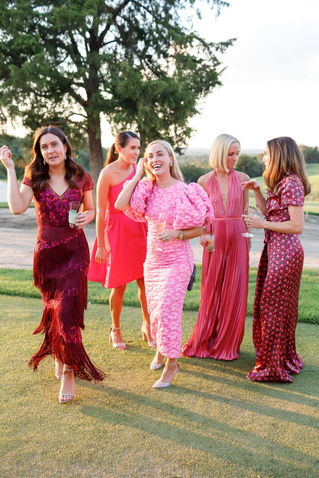Group of women in colorful dresses laughing together outdoors during cocktail hour