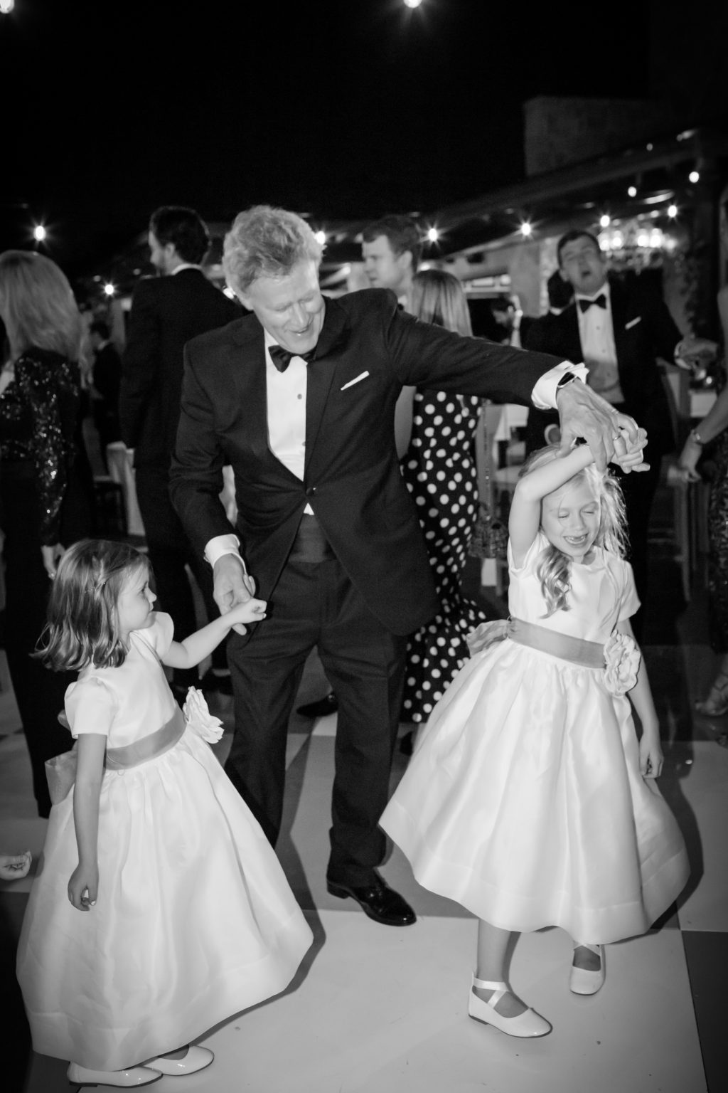 Man in a tuxedo laughing and dancing with young girls during a Dallas wedding celebration