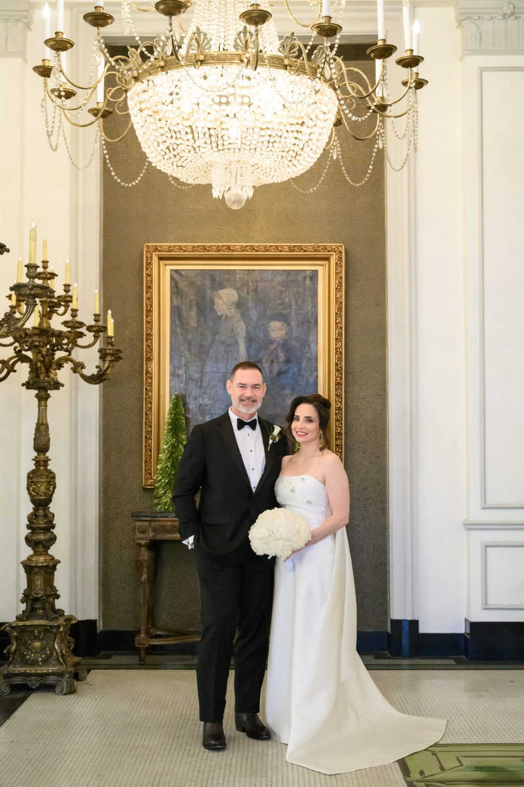 Bride and groom posing beneath a chandelier inside Peacock Alley at The St. Anthony Hotel