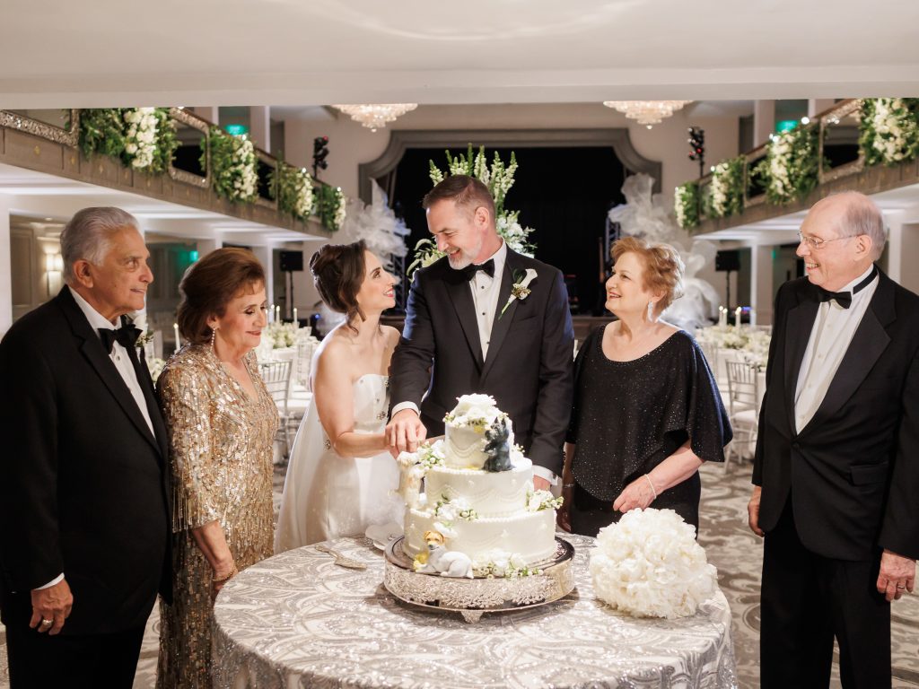 Bride and groom cutting their wedding cake surrounded by family at The St. Anthony Hotel
