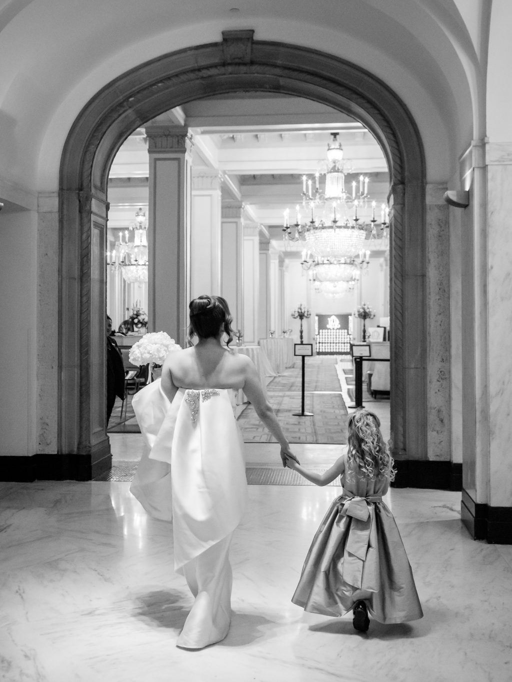 Black and white photograph of the bride walking through The St. Anthony Hotel with a flower girl