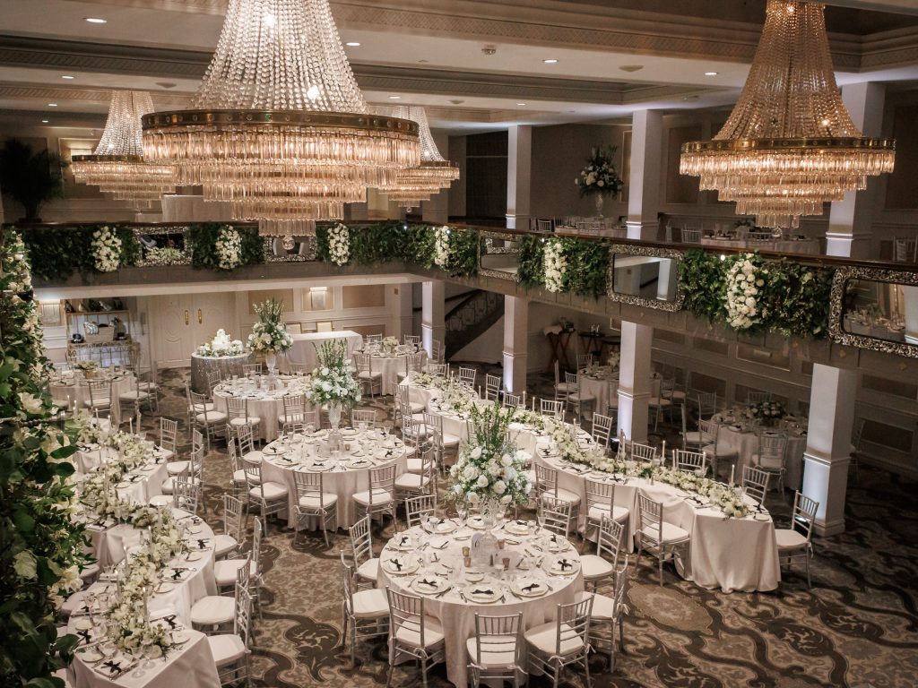 Wedding reception with white flowers, greenery and crystal chandeliers at the Anacacho ballroom at the St. Anthony hotel planned by Wilkinson Rhodes