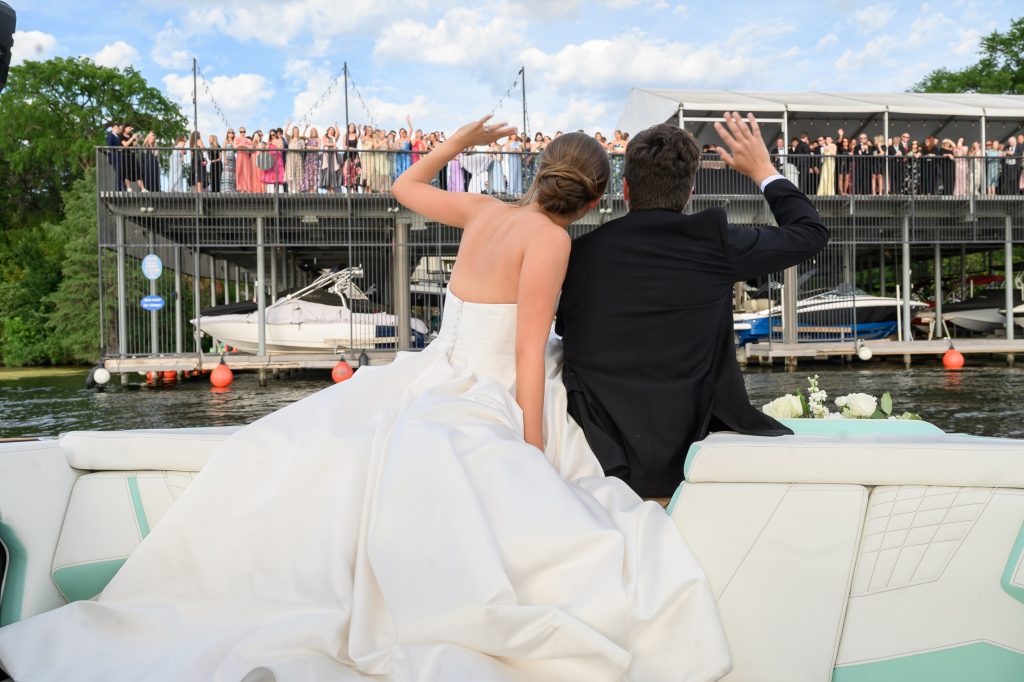 Maddy and Will wave to guests as they arrive by boat for their Westwood Country Club wedding reception