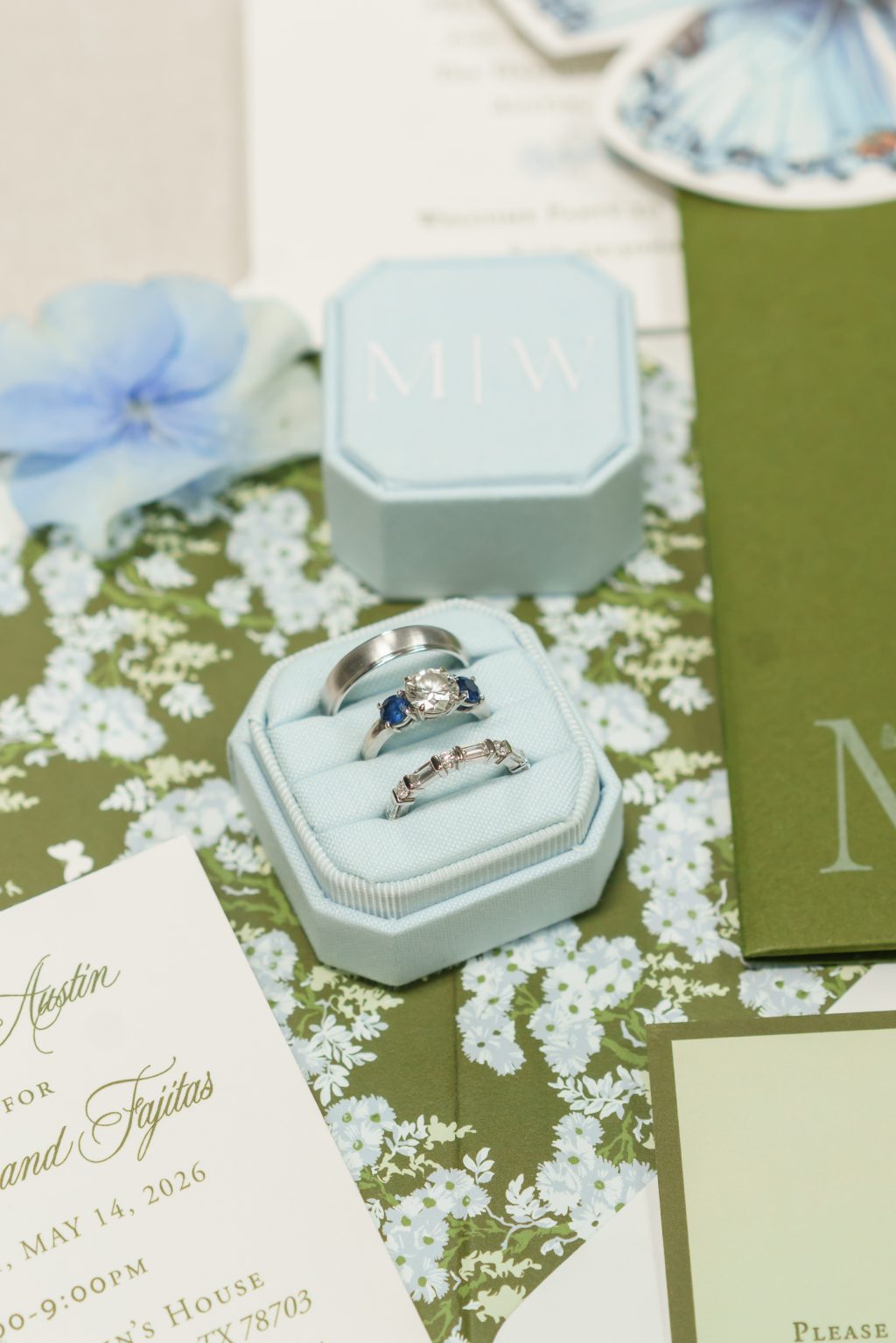 Wedding rings displayed with blue butterfly stationery and classic green invitation details