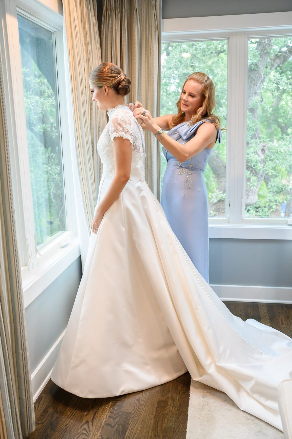Bride’s mother helps her dress beside a window in the Austin home where she grew up