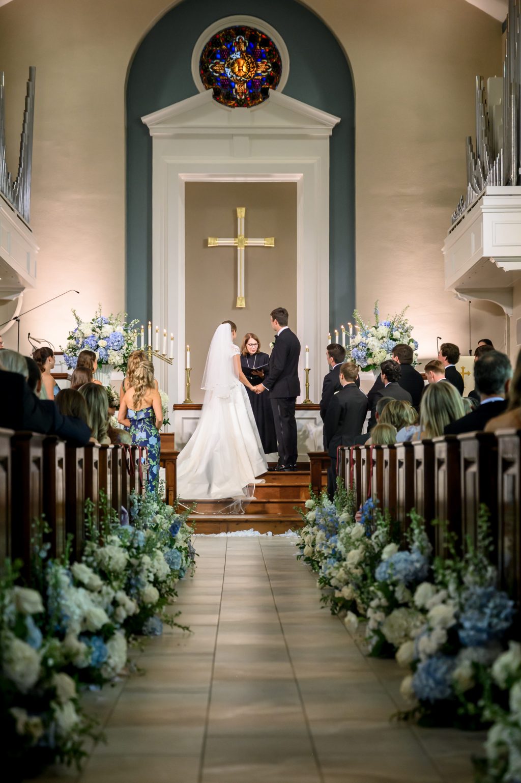 Bride and groom stand at the altar beneath a gold cross during their church wedding