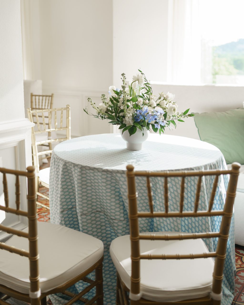 Intimate cocktail table with blue linen, gold chairs, and a blue and white floral arrangement