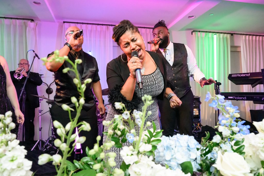 Matchmaker Band performs behind blue and white flowers during the wedding reception