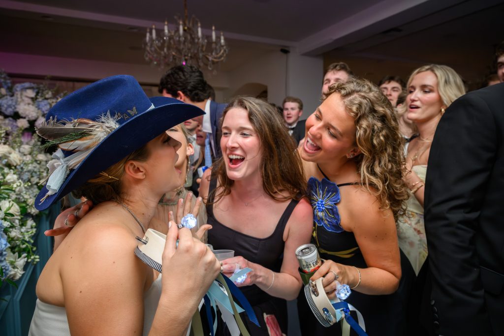 Bride laughs with friends wearing playful hats on the dance floor
