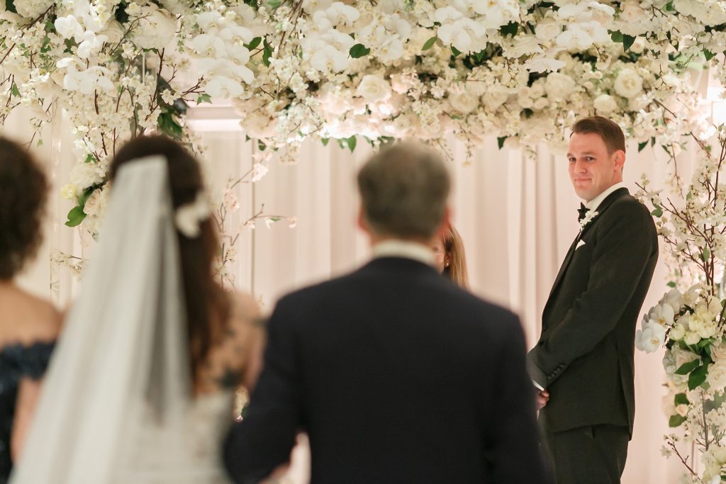 Groom watching the bride during a floral indoor wedding ceremony at Four Seasons Austin