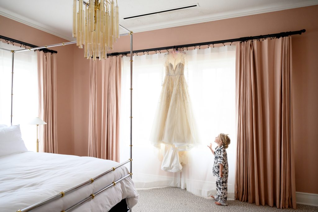 Wedding dress hanging in the pink bedroom of the Mr. and Mrs. Perry Suite at Commodore Perry Estate with the little flower girl looking up at it