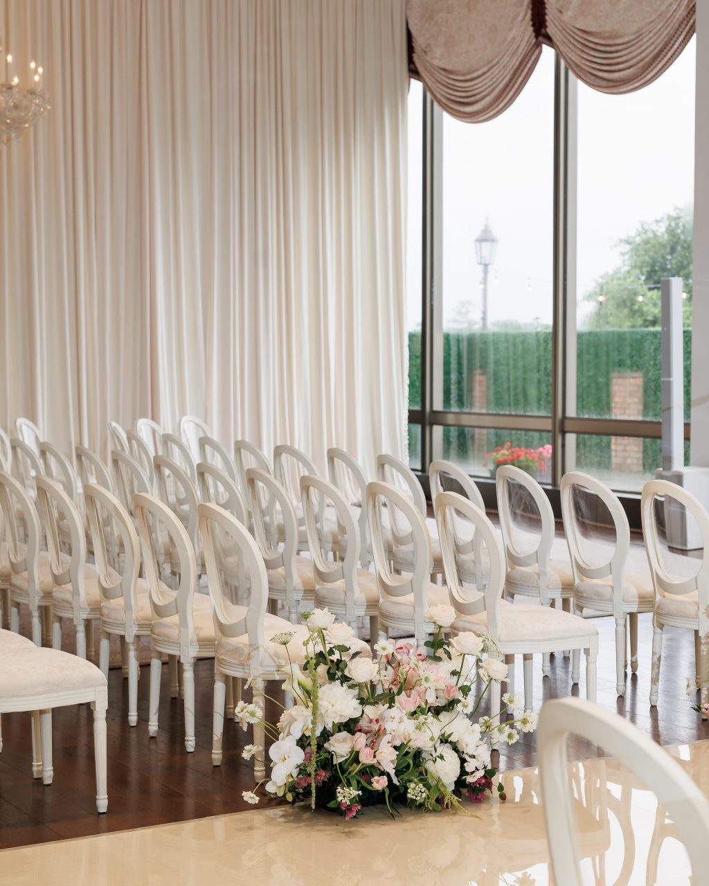 Wedding ceremony aisle with floral arrangements beside the windows at River Oaks Country Club